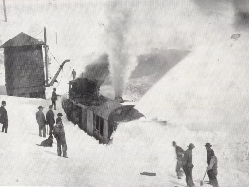 Men attempt to dig out a railroad locomotive from deep snow.