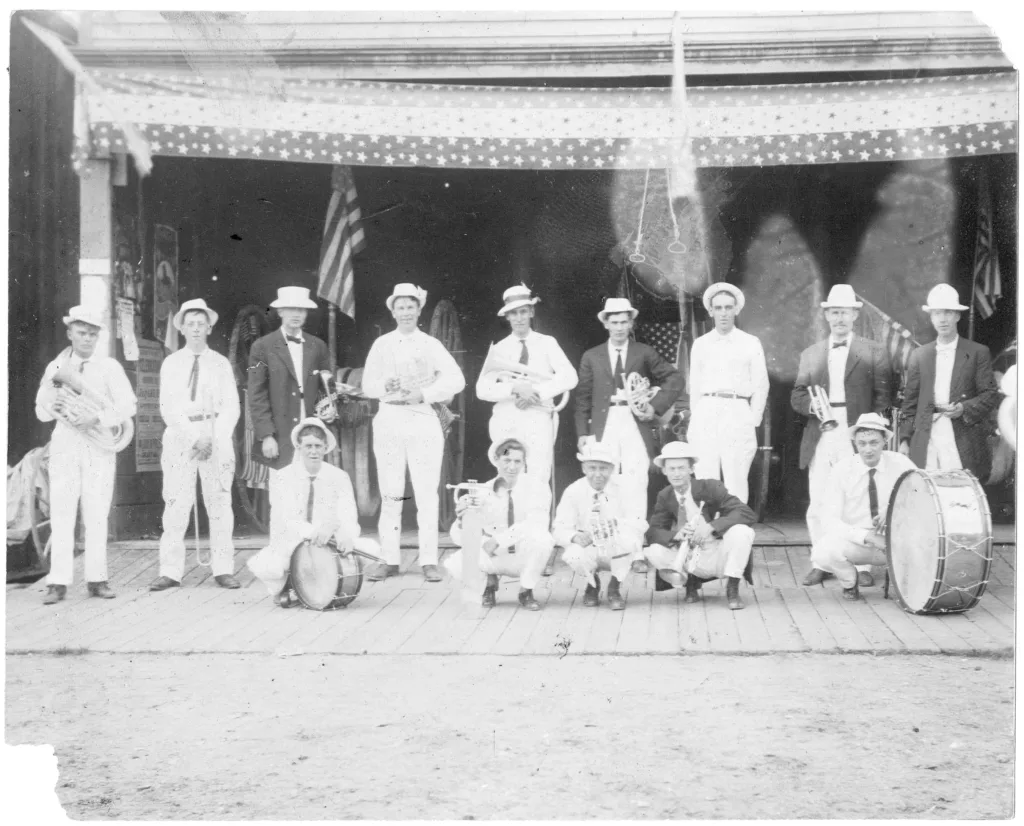 Breckenridge Band members kneel or stand with their musical instruments on the wooden sidewalk in front of Fireman's Hall on Main Street, Breckenridge, Colorado. Circa 1890s-1900s