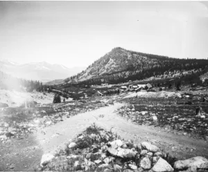 Two roads cross in the foreground with a large mountain in the background. In the center of the photo sits a small mining camp.