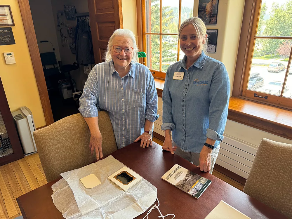 Becca Kohl and Kris Ann Knish stand next to a table in the Breckenridge History Archives. On the table sits the 1862 ambrotype.